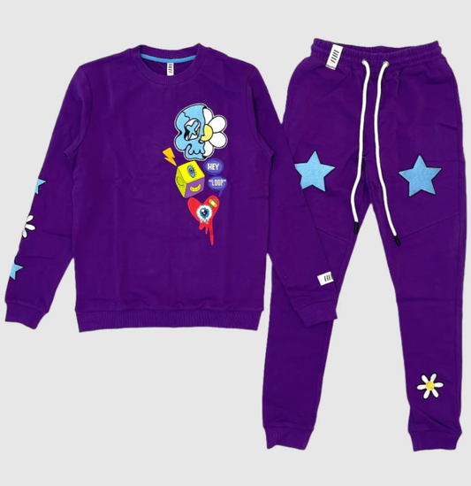 Purple two-piece jogger set featuring a graphic sweatshirt with cartoon skull, dice, flower, and heart designs, paired with matching jogger pants decorated with blue star patches and daisy graphics
